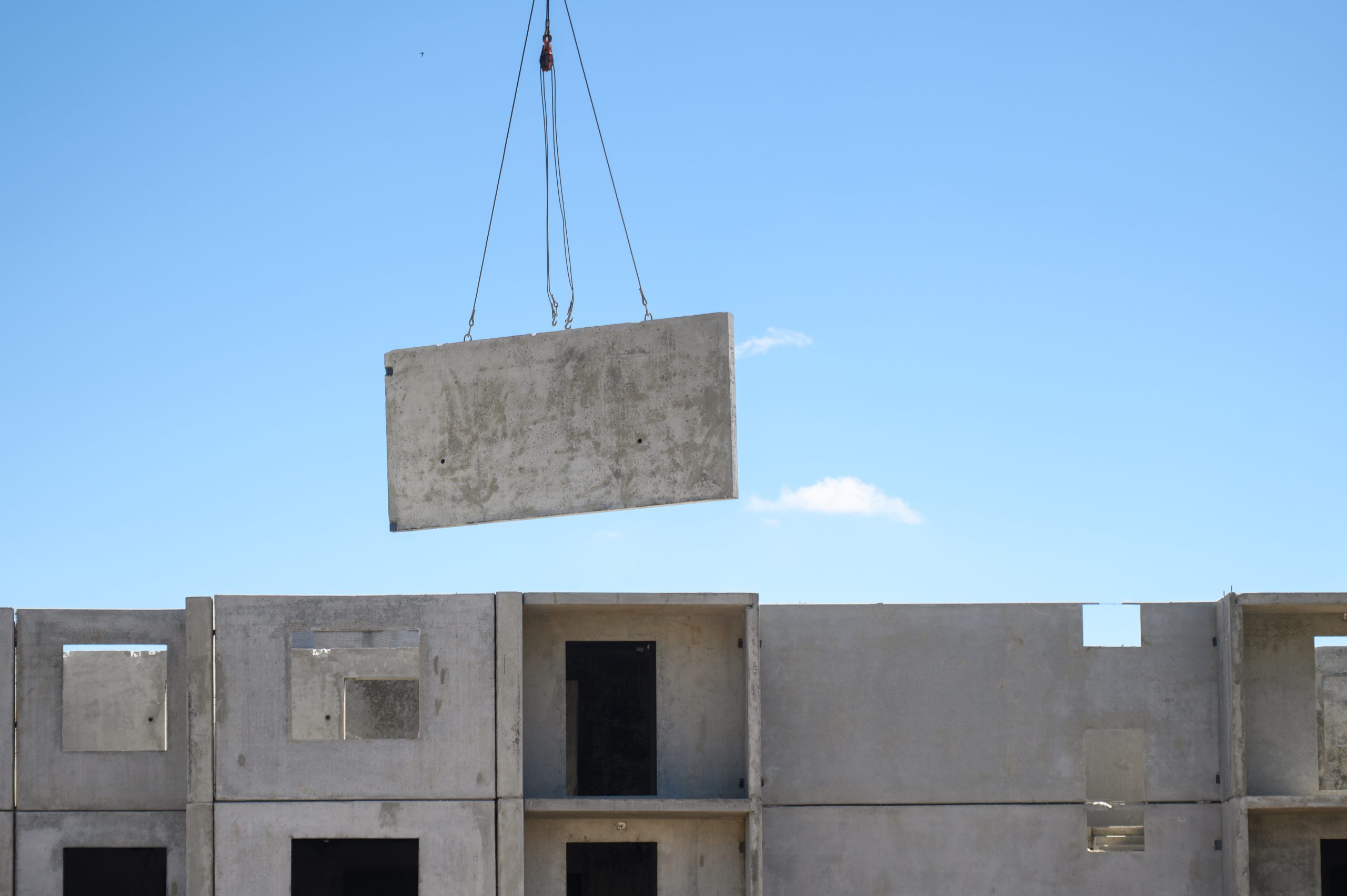Construction crane on cables lifts panel for construction of multi-apartment residential building, office building against blue sky. Construction concept. Construction crane on cables lifts panel for construction of multi-apartment residential building, office building against blue sky. Construction concept