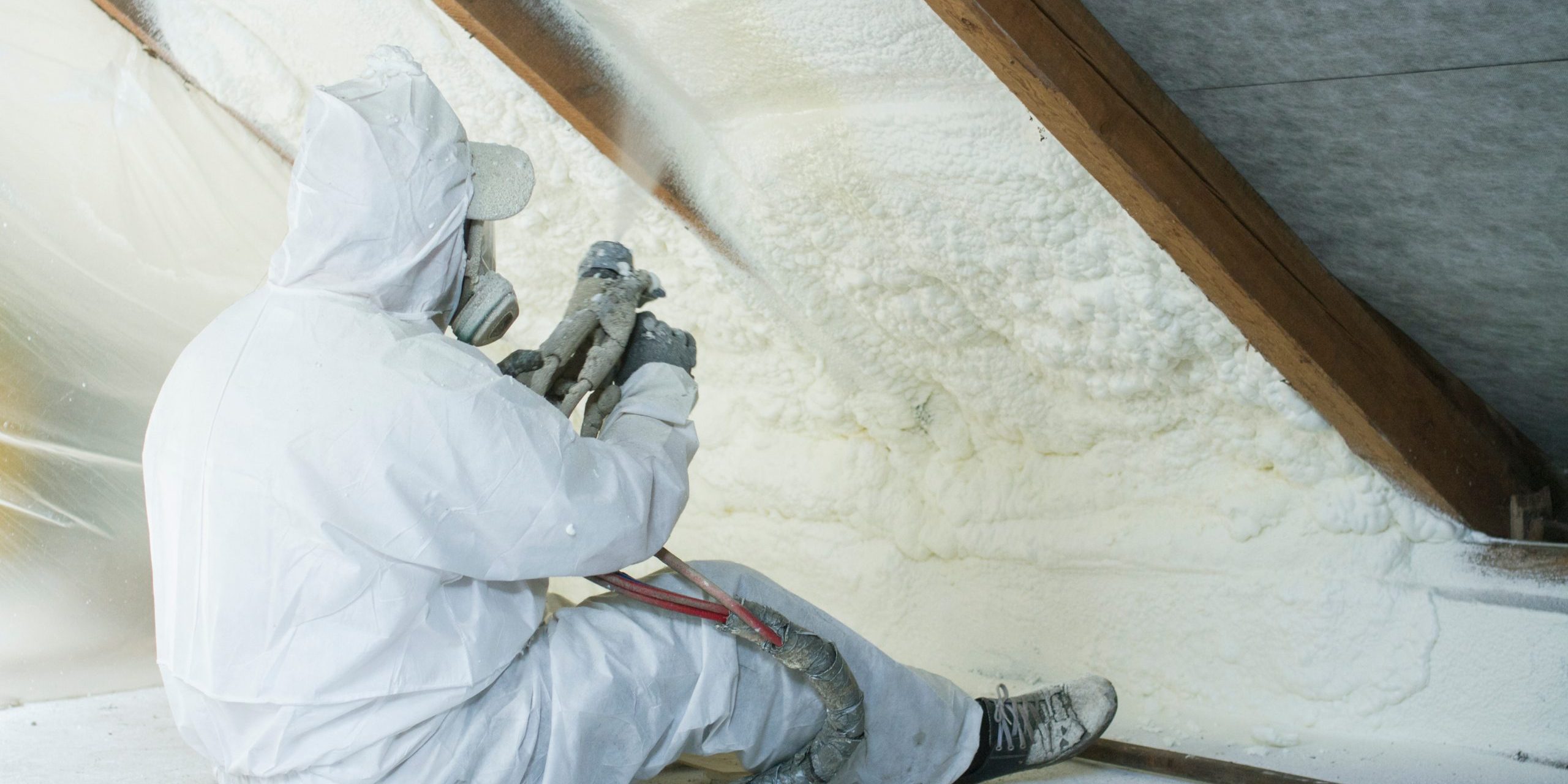 spray polyurethane foam for roof - technician spraying foam insulation using plural component gun for polyurethane foam, inside